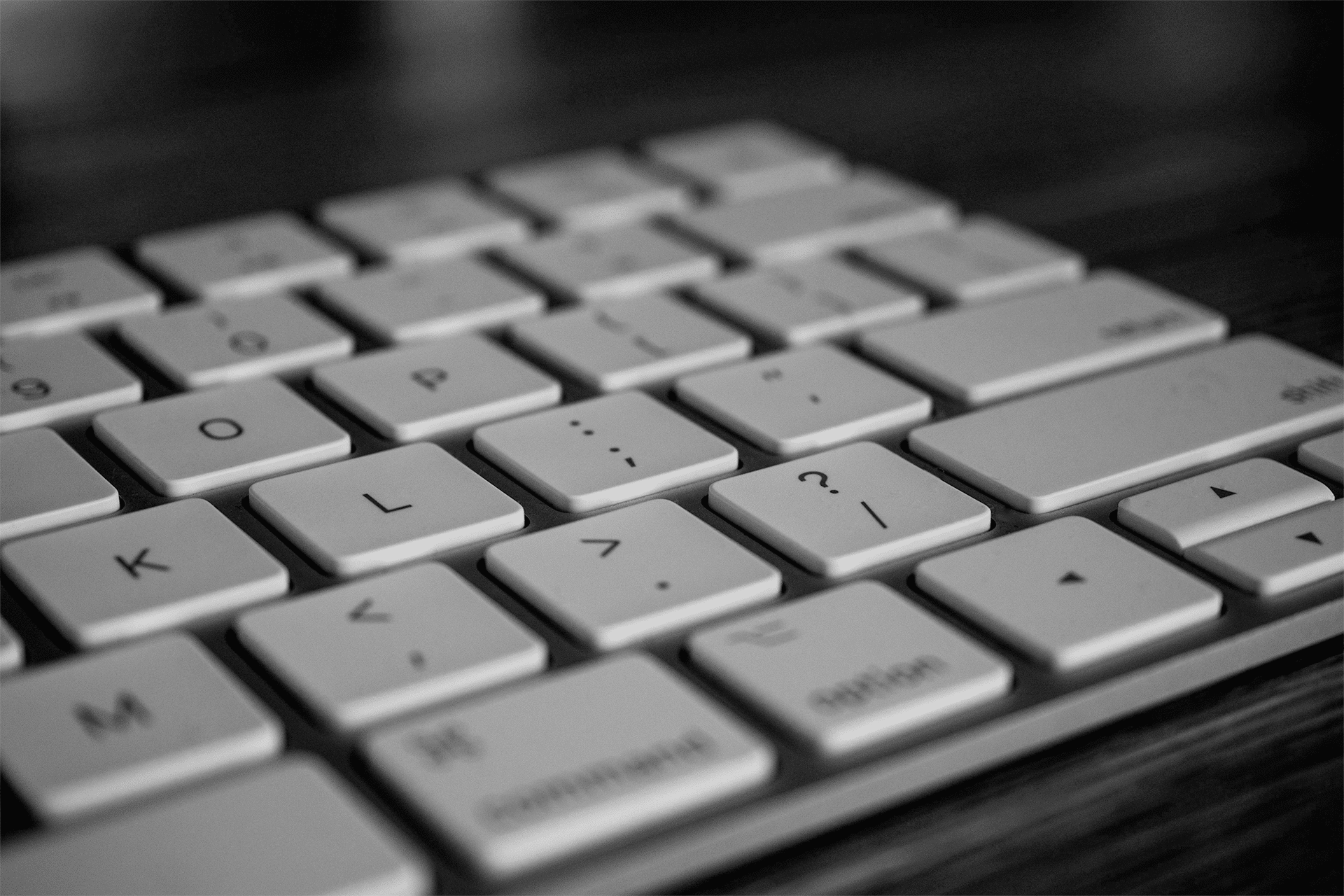 A close-up, black and white image of a Magic Keyboard focusing on the central letter and symbol keys, with shallow depth of field and a blurred background.