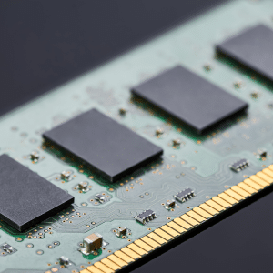 A close-up view of a computer RAM module, highlighting four black memory chips on a green circuit board with gold connector pins—an example of hardware impacted by the recent RAM price surge.