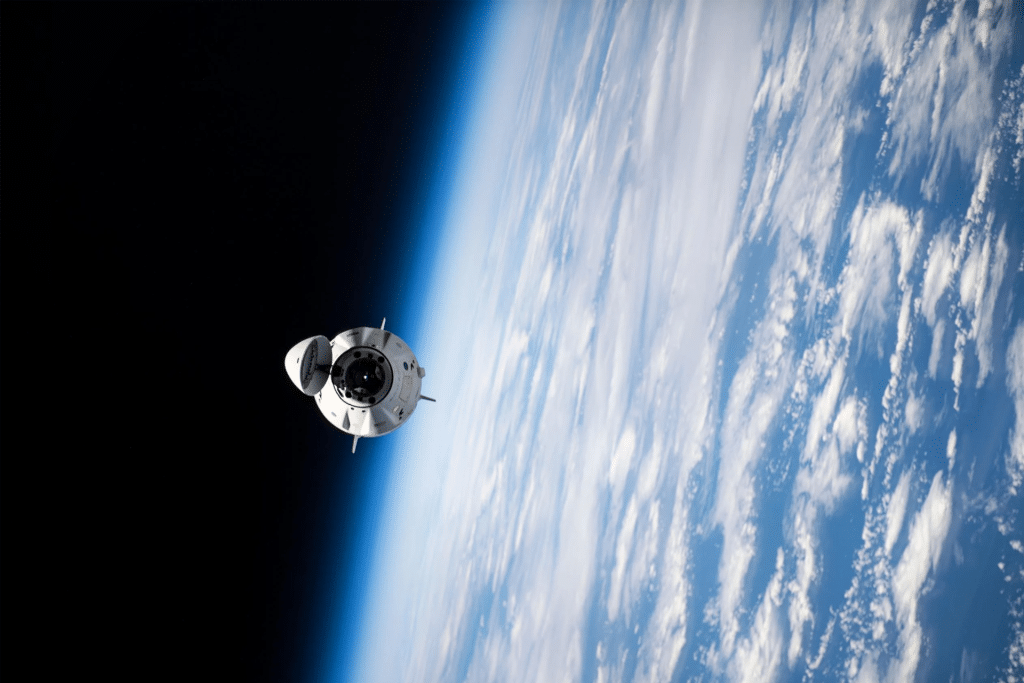 A SpaceX spacecraft orbits above Earth, with the planet’s blue atmosphere and white clouds visible below and the darkness of space in the background—hinting at possibilities like a potential SpaceX 2026 IPO.