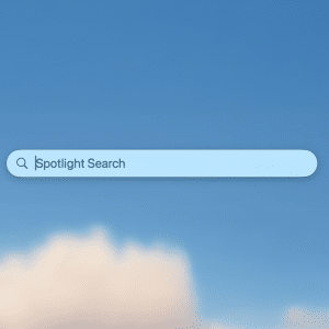 A Spotlight Search bar appears centered on a clear blue sky background with a few soft clouds at the bottom, perfect for discovering new Spotlight search tips on your Mac.