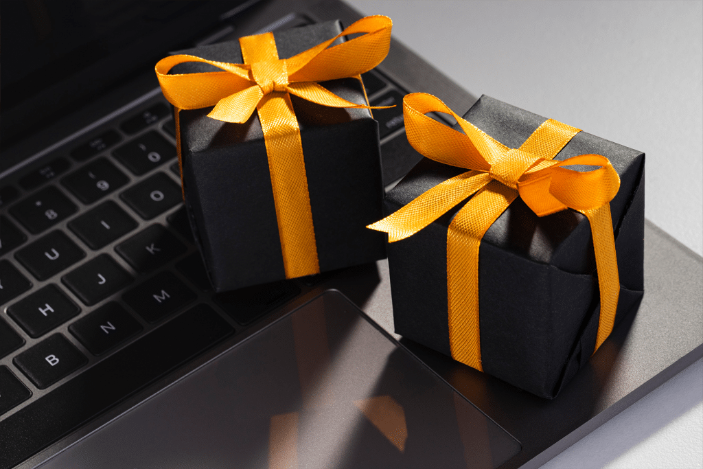 Two small black gift boxes with yellow ribbons sit on the keyboard and trackpad of a laptop, evoking a blend of technology and gifting—perfect inspiration for ai holiday shopping this season.