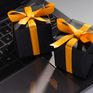 Two small black gift boxes with yellow ribbons sit on the keyboard and trackpad of a laptop, evoking a blend of technology and gifting—perfect inspiration for ai holiday shopping this season.