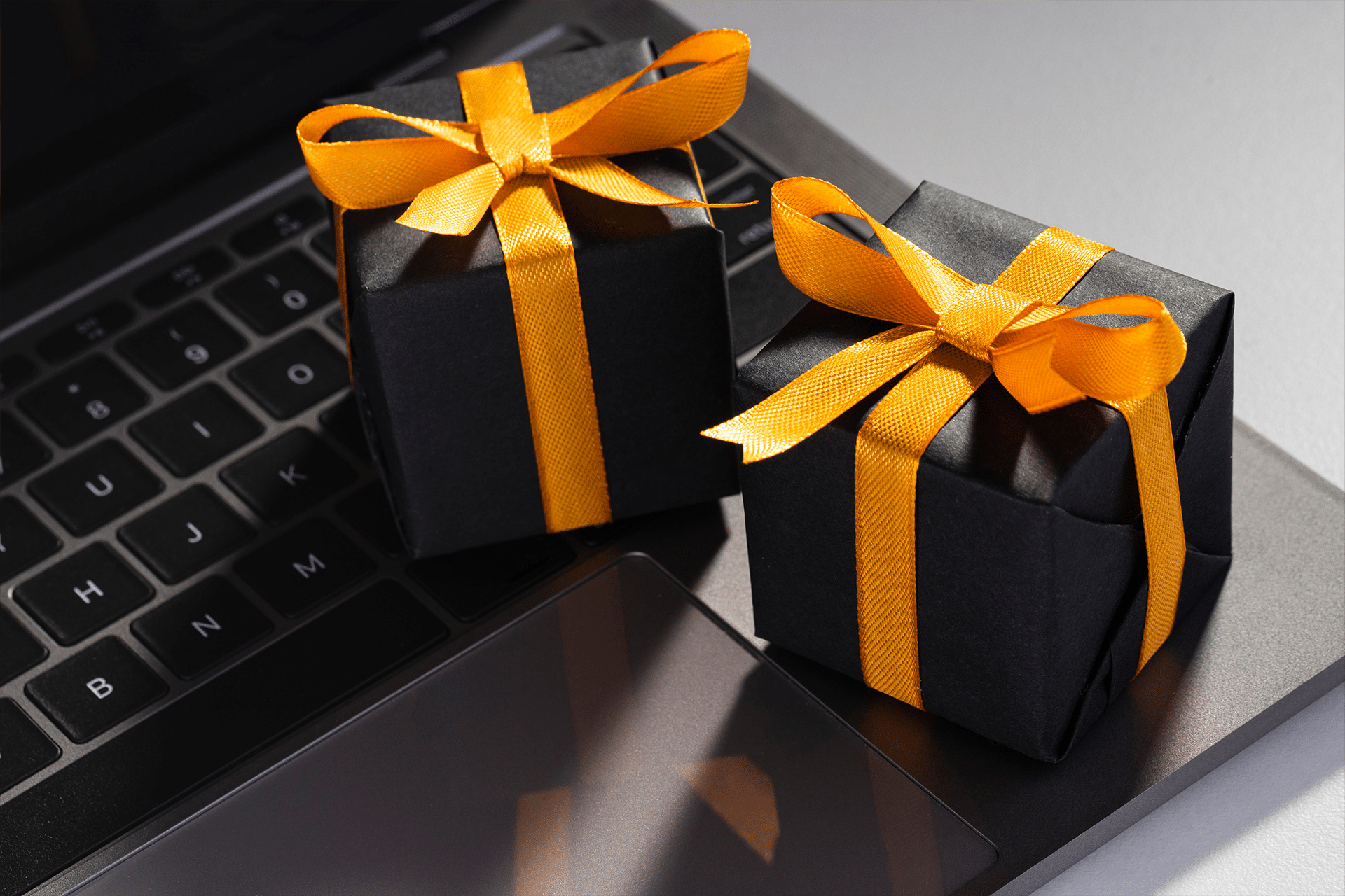 Two small black gift boxes with yellow ribbons sit on the keyboard and trackpad of a laptop, evoking a blend of technology and gifting—perfect inspiration for ai holiday shopping this season.