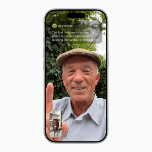 A smiling older man in a flat cap is on a Facetime video call, holding up his index finger. He is outside with greenery behind him. A small inset shows another smiling man on the call. Text instructions appear at the top of the screen.