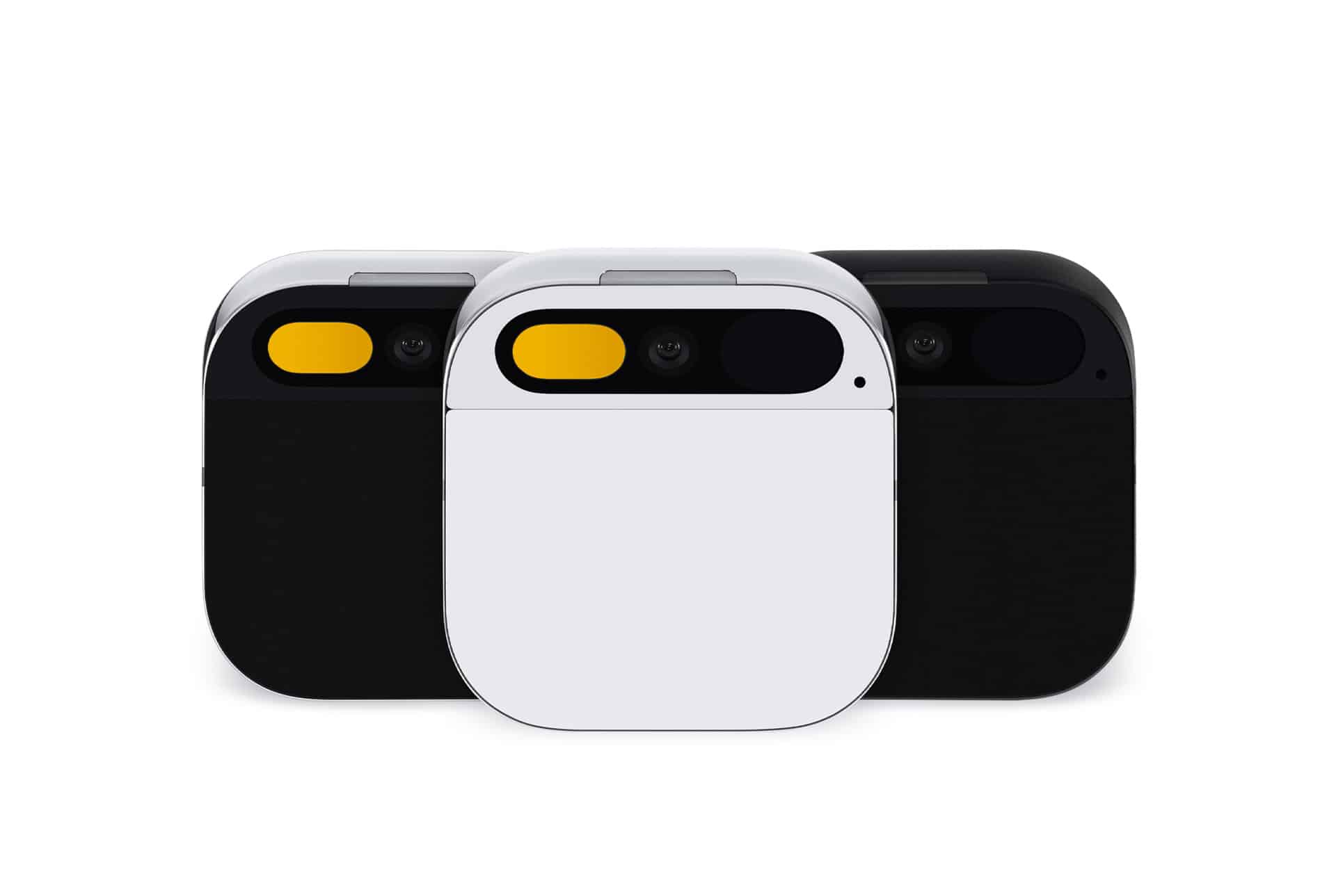 Three compact, rectangular devices with rounded corners are shown in black, white, and dark gray. Each AI Pin features a small camera lens and a yellow accent on the upper left corner of the front panel.