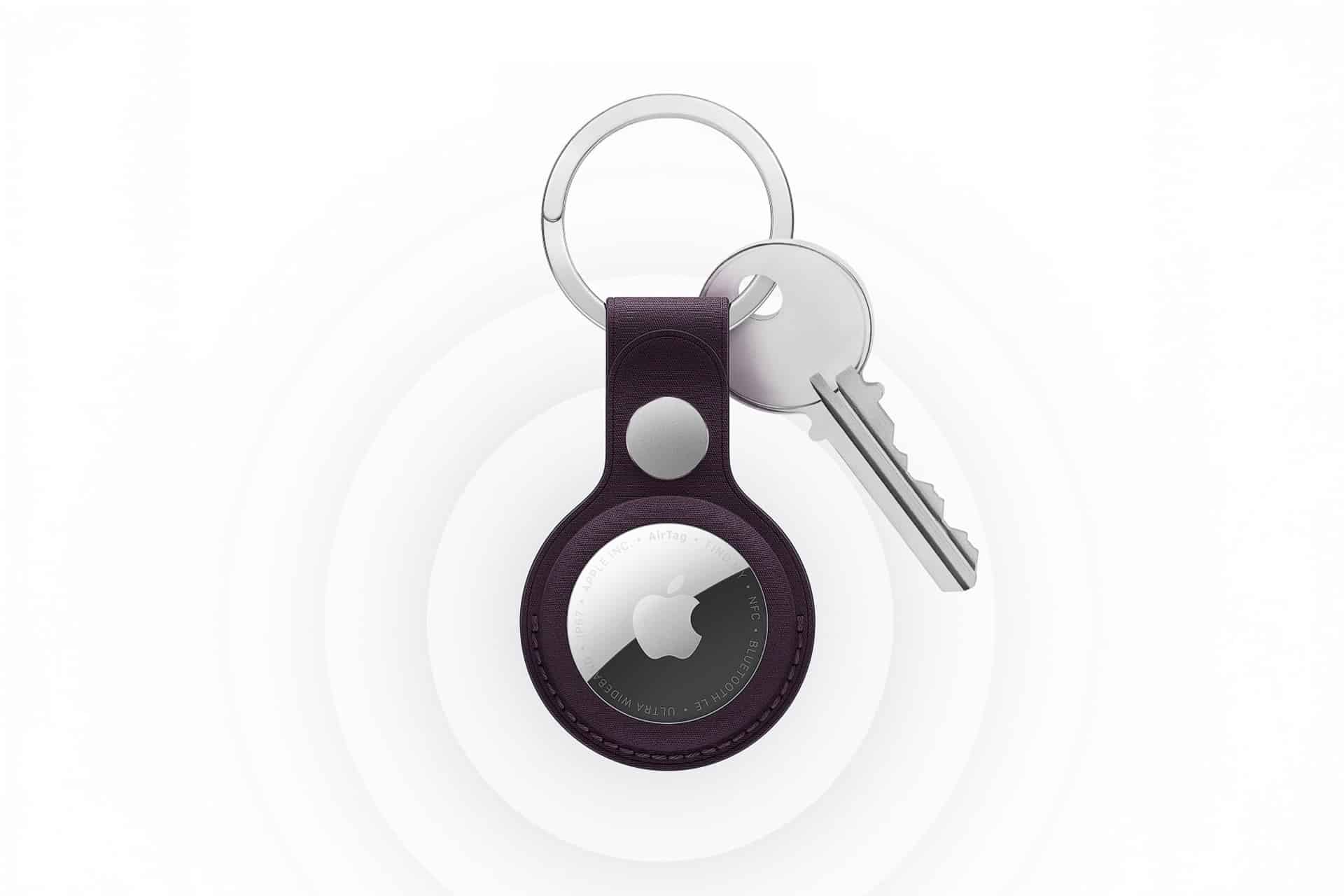 A silver key and a keyring with a new AirTag in a black leather holder, displayed on a white background with circular ripple patterns.