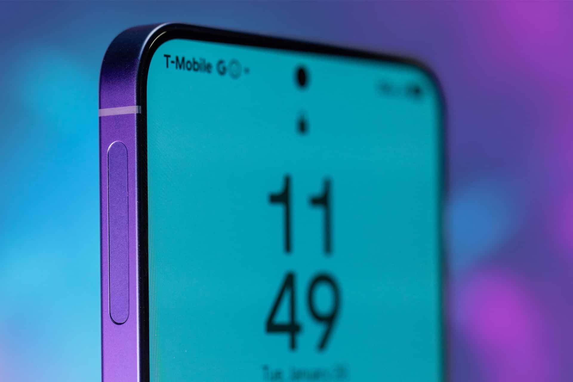 Close-up of a modern smartphone with a purple frame, displaying the time 11:49 and T-Mobile 5G signal. The iOS vs Android debate comes to mind as the phone shows a small camera cutout, with a blurred purple and blue background.