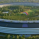 Aerial view of Apple Park, a circular building surrounded by trees, with a large colorful rainbow structure and green lawns inside the central courtyard—a testament to innovation fueled by notable Apple acquisitions.