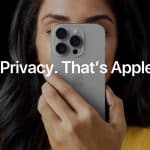 Apple Privacy - A person holds an iPhone in front of their face, partially covering it. Overlaid text reads, "Privacy Audit. That’s Apple." The person has long dark hair and is wearing a yellow top.