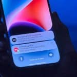 iPhone held in a hand displaying Emergency SOS via Satellite and iPhone Crash Detection alerts on the lock screen.