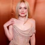 Dakota Fanning, with straight blonde hair, wears an off-shoulder sparkling light pink dress and a necklace. She poses before a copper background, softly smiling at the camera—promoting her role in the Apple TV New Thriller.