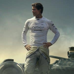 A man in a white racing suit stands confidently before a Formula 1 car, his suit unzipped to the waist and hands on hips, gazing to the side as dramatic clouds loom—captured with cinematic flair in Apple Creator Studio.