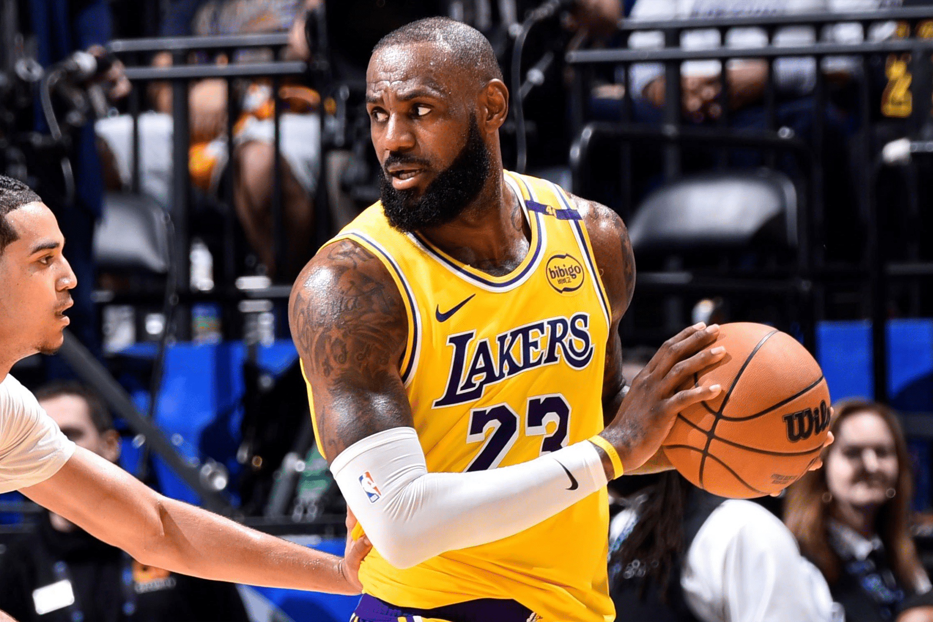 A basketball player in a yellow Lakers jersey with the number 23 holds a basketball, showcasing Vision Pro-level focus as he looks to pass while a defender approaches during the game.