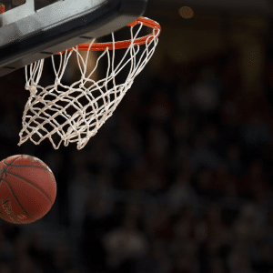A basketball is about to go through a hoop with a white net during a game, as seen on Apple TV NBA League Pass, with a blurred crowd in the background.