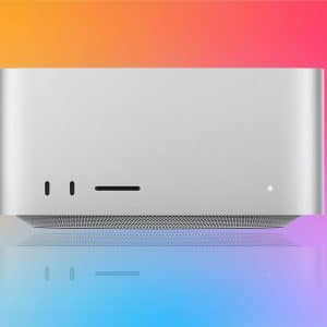 A silver Apple desktop computer with a minimalist design is shown against a vibrant gradient background of orange, pink, and blue, making it perfect for a sleek Mac Studio Setup. The Apple logo is visible in the lower right corner.