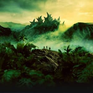 Apple TV Monarch - Three people stand in a lush, misty jungle facing a distant mountain with jagged, fantastical rock formations under a dramatic yellow-green sky. Dense vegetation and palm trees surround them in this cinematic scene inspired by Apple TV Monarch.