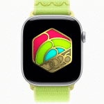 An Apple Watch with a yellow-green band displays a colorful hexagonal design featuring gold, pink, red, and green elements, with "2026" in gold at the bottom center—perfect for fitness motivation and style.