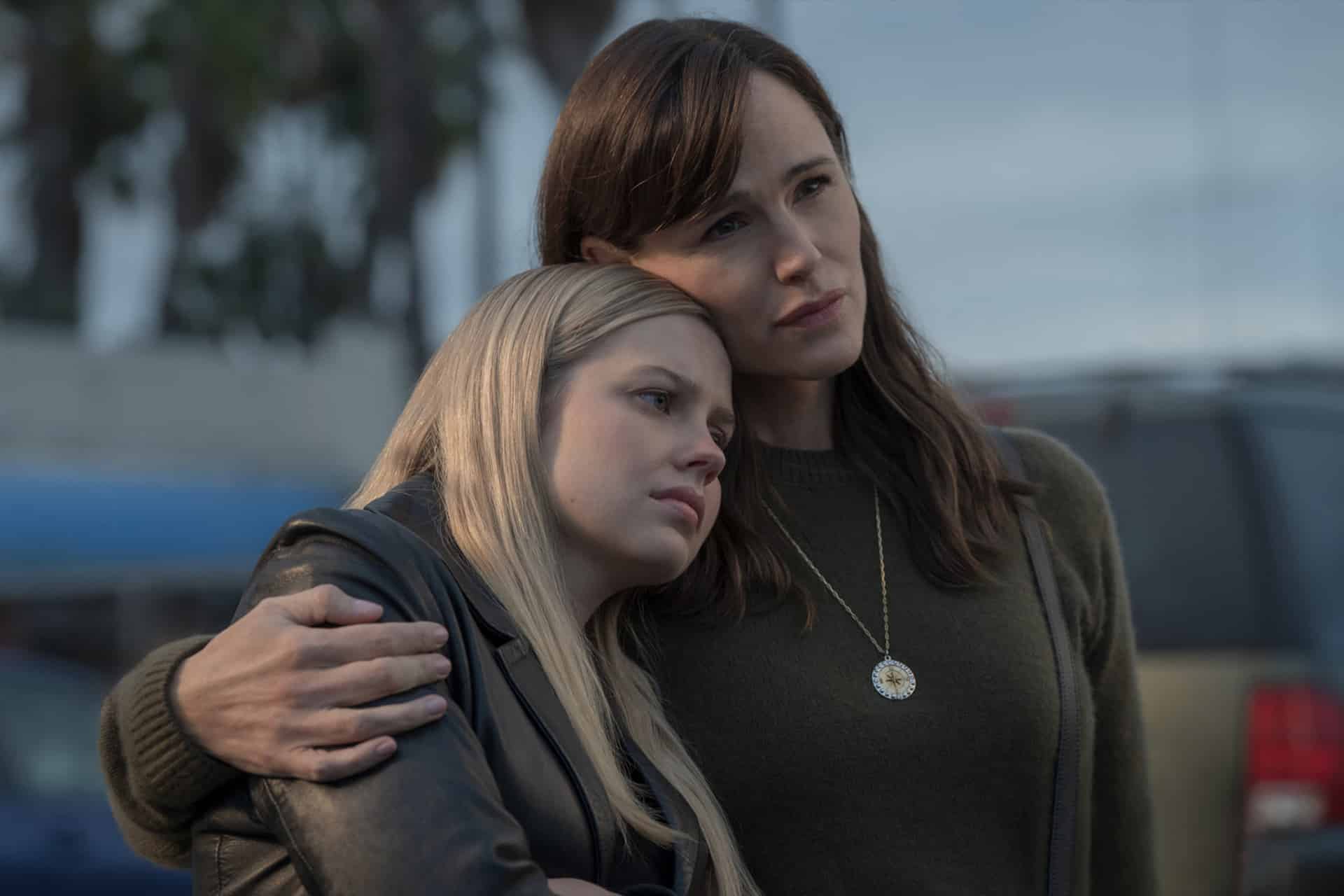 A woman with brown hair hugs a younger blonde woman, who rests her head on the woman's shoulder. They both look thoughtful and serious—perhaps reflecting on events from Last Thing Season 2—as they stand outdoors with cars and trees behind them.
