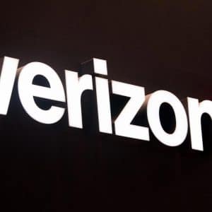 The illuminated Verizon logo with white letters and a red checkmark is displayed on a dark background, perfect for showcasing the latest iPhone Verizon offers.