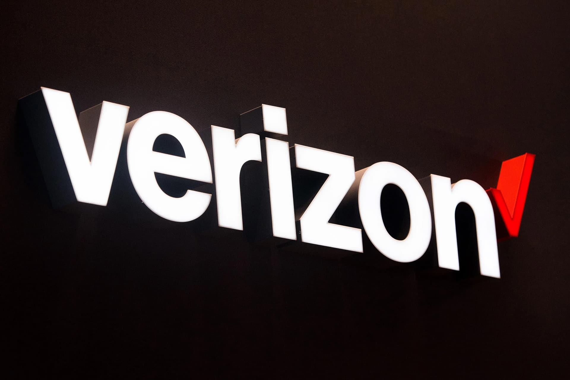 The illuminated Verizon logo with white letters and a red checkmark is displayed on a dark background, perfect for showcasing the latest iPhone Verizon offers.