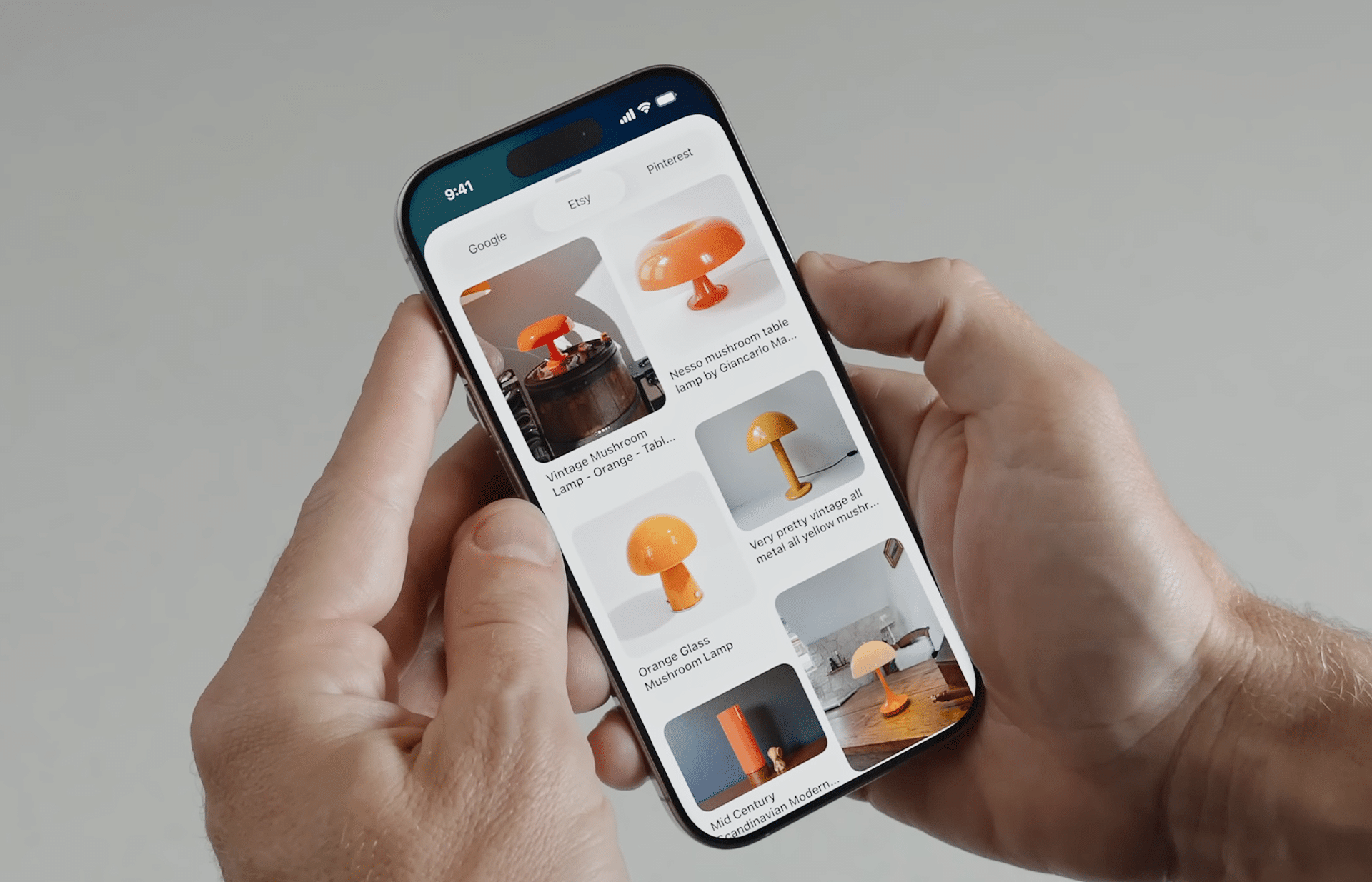 A person holds a smartphone displaying images of orange mushroom-shaped lamps, searching for lamp ideas. The scene subtly illustrates How Visual Intelligence Works on iPhone, with a plain and neutral background.