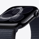 A close-up of a black smartwatch with a dark reflective screen displaying abstract, circular patterns, attached to a textured dark fabric strap, shown against a plain light background—perfect for showcasing Apple Watch screen care.
