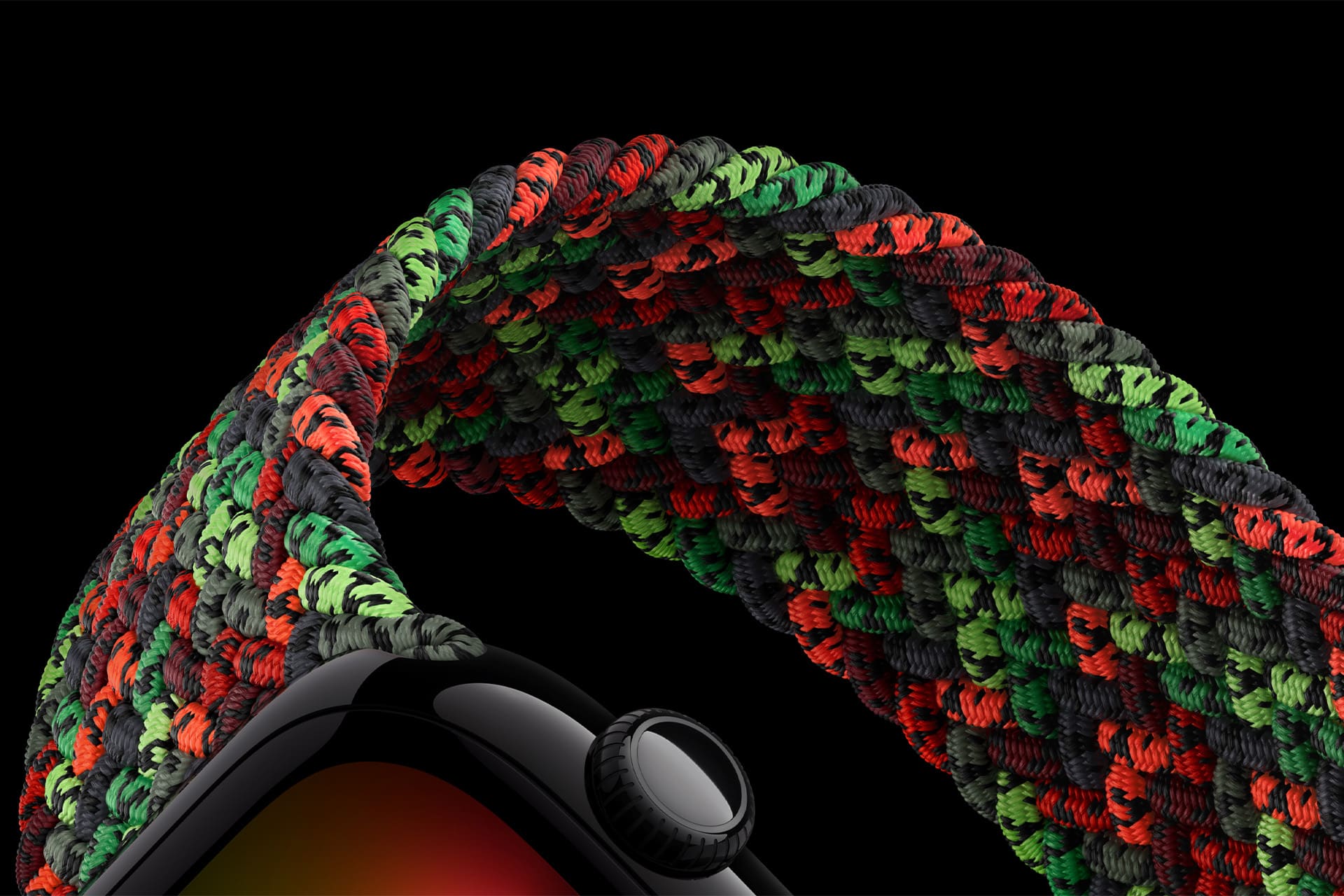 Close-up of an Apple Watch featuring the Black Unity Band—a braided solo loop in black, red, and green—against a black background. The image highlights the band’s vibrant pattern and unique texture.