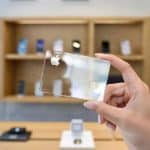 A hand holds a transparent digital-first credit card with the Apple logo in a modern tech store, where shelves display various electronic devices in the background.
