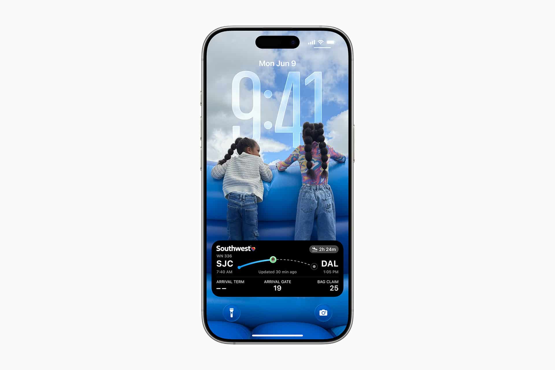 A smartphone displaying its lock screen, featuring a photo of two children looking over a blue railing and an iPhone Apps widget showing a Southwest flight from SJC to DAL.