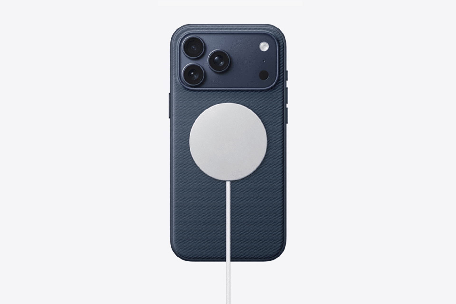 A dark blue iPhone 17 with three rear cameras is connected to a circular wireless charger attached to its back. The white charger, cable extending downward, powers up the device while addressing static speaker noise issues.