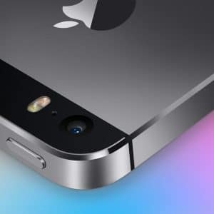 Close-up of the top back corner of a black iPhone old model, showing the camera, flash, and part of the Apple logo, with a colorful gradient background and a small white Apple logo in the lower right corner.