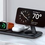 A wireless charging station on a marble surface holds a smartwatch, wireless earbuds, and a smartphone displaying iPhone StandBy with the clock and San Diego weather (70°F, mostly sunny), charging all devices at once.