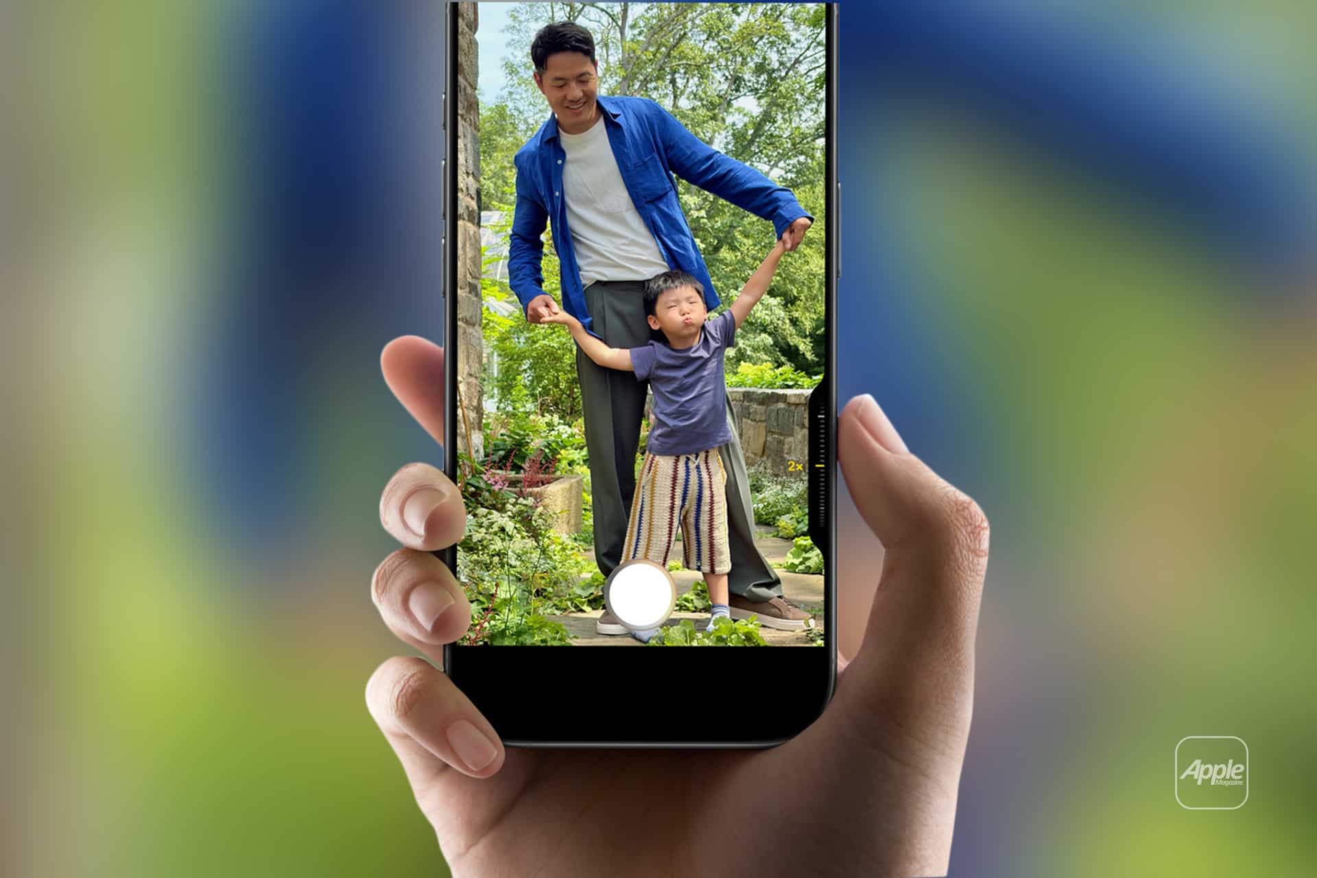 iPhone Video - A hand holds a smartphone displaying an iPhone Video being taken of a smiling man in a blue jacket holding hands with a young child in a striped skirt, standing together outdoors in a lush garden.