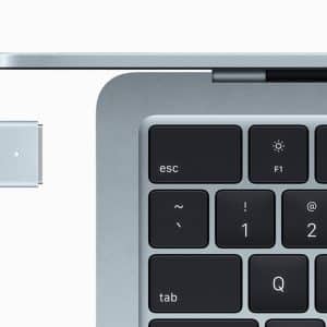 Close-up of a laptop keyboard and screen, partially open, with a magnetic charging cable near the port—highlighting MacBook Plugged Safe features for optimal MacBook Battery Health. The escape, tab, and function keys are visible.