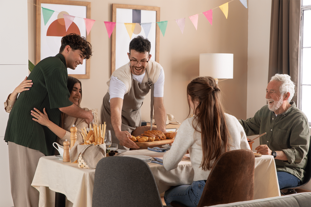 A group of five people gather around a dining table, smiling and enjoying a meal together. Colorful bunting decorates the room, while an Apple Music guest playlist adds to the festive and warm atmosphere.