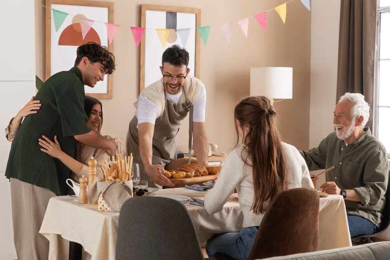 A group of five people gather around a dining table, smiling and enjoying a meal together. Colorful bunting decorates the room, while an Apple Music guest playlist adds to the festive and warm atmosphere.