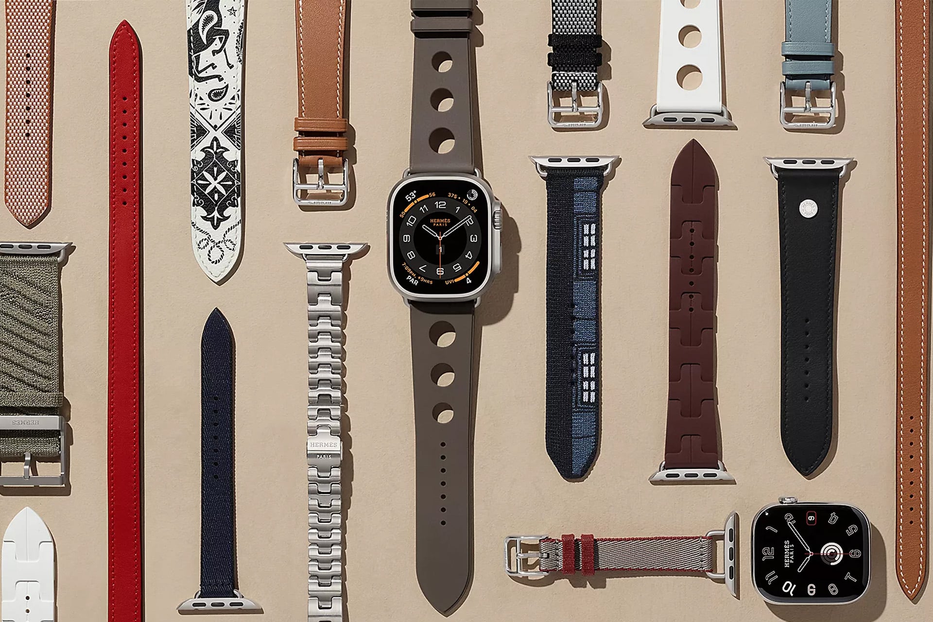 A selection of Apple Watch bands in different colors, materials, and styles—including options that complement various skin tones—are arranged neatly on a tan background, with an Apple Watch Ultra and an additional watch face displayed among them.