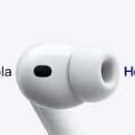 Close-up of a white wireless earbud, highlighting airpods translation, with "Hola" on the left in gray and "Hello" on the right in a blue, purple, and pink gradient against a light gray background.