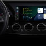 Close-up of a car dashboard display featuring Apple CarPlay smart home controls, a digital schedule, and climate settings next to the steering wheel. The screen showcases colorful icons and clear text.