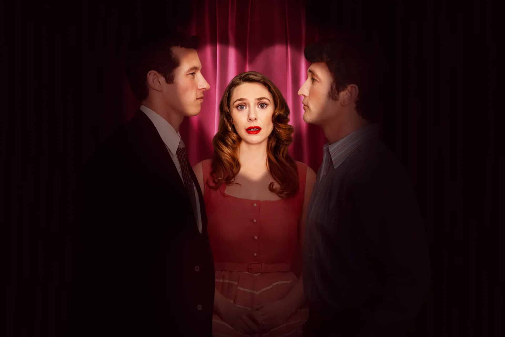 A woman in a red dress stands between two men facing her, with dramatic lighting and a dark red curtain backdrop. She looks forward with a concerned expression while the men gaze at each other in this tense Eternity Movie on Apple TV.