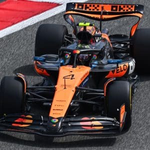 An orange and black Formula 1 car races on the track, showcasing the number 4 and sponsors' logos. The driver is visible in the cockpit, with a red and white curb on the left—perfect for watching in stunning detail on Apple TV IMAX.