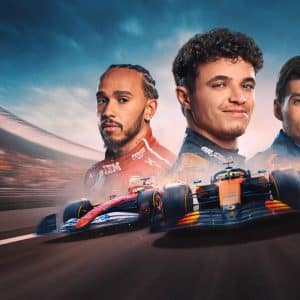 Three Formula 1 drivers stand side by side, with race cars speeding on a blurred racetrack beneath them. The background features stadium lights and a dramatic sky, capturing the excitement of Apple TV F1 coverage.