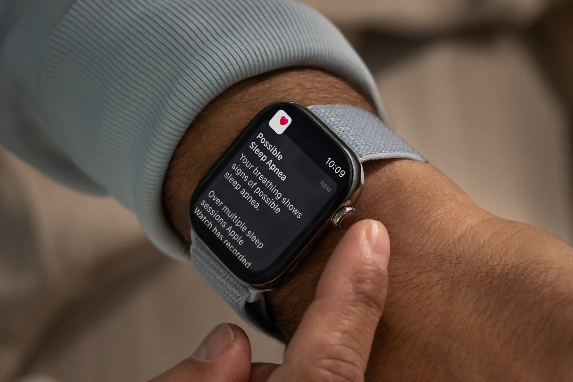 Caregiver Apple Watch - A close-up of a person’s wrist wearing a smartwatch with a light blue band, displaying a health notification about possible symptoms of atrial fibrillation and sleep data, highlighting apple accessibility features for Older Adults.
