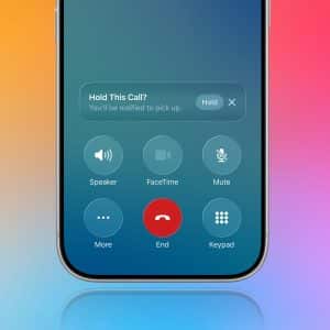 A smartphone screen displays an active call with options like speaker, FaceTime, mute, more, end, and keypad. A colorful gradient background is visible as a Hold Assist Detection notification says, “Hold This Call? You’ll be notified to pick up.”.