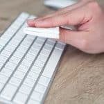 A person cleans a white Magic Keyboard with a folded white cloth on a wooden desk.