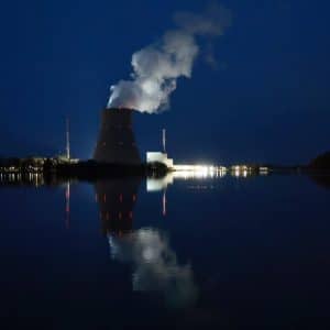 A nuclear power plant at night emits white steam from its cooling tower, brightly lit and reflected in calm water—an image echoing the transformative force of the AI Industry Power shaping our technological landscape.
