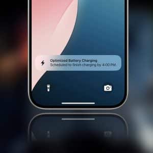Close-up of a smartphone screen displaying a smart charging notification, with optimized battery charging set to finish by 4:00 PM. The flashlight and camera icons appear at the bottom of the screen.