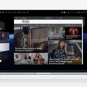 A MacBook displays a web browser open to an Apple news site, with articles and images. App thumbnails line the left side, showcasing the Stage Manager feature, while the Apple logo sits in the top right of the white Mac desktop background.