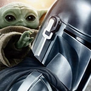 A close-up of The Mandalorian in metal armor with Grogu, also known as Baby Yoda, peeking over his shoulder and reaching forward, set against a blurred, snowy background from the hit Disney+ Star Wars series.