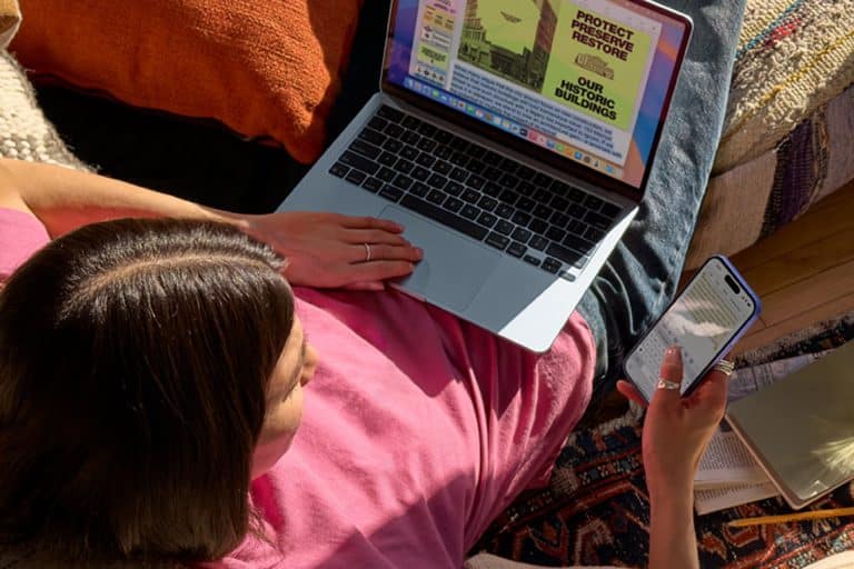 A person in a pink shirt sits on a couch using a laptop and holding a smartphone, reflecting teenage tech preference. The laptop displays a colorful page about protecting historic buildings as sunlight streams onto the cozy scene.